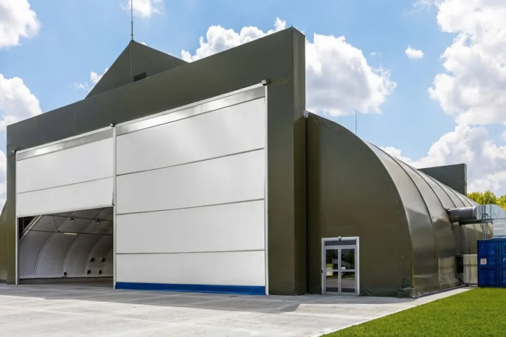 Hangar materiałowy w kolorze oliwkowym z jednym skrzydłem bramy otwartym